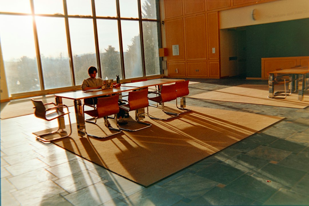 University student studying at a desk near large library windows, illustrating research on AI study assistants and student engagement.