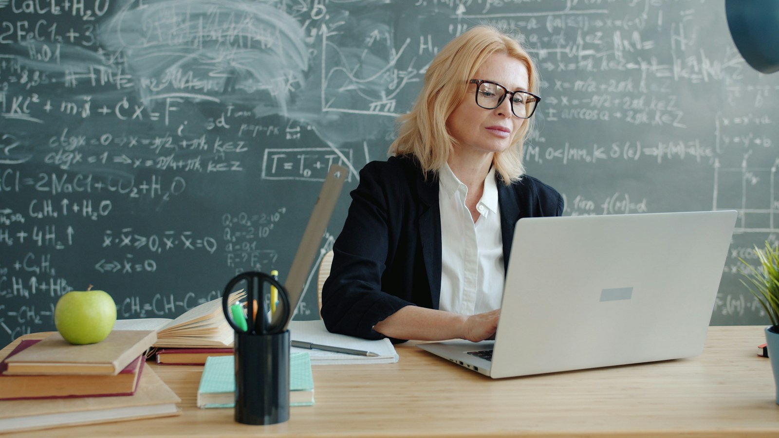 Teacher using a laptop in a classroom, illustrating AI teacher training and educational technology