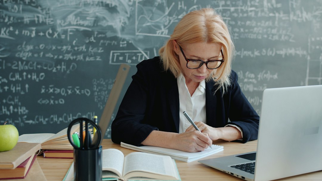 Teacher working at a desk with a laptop and notes in a classroom